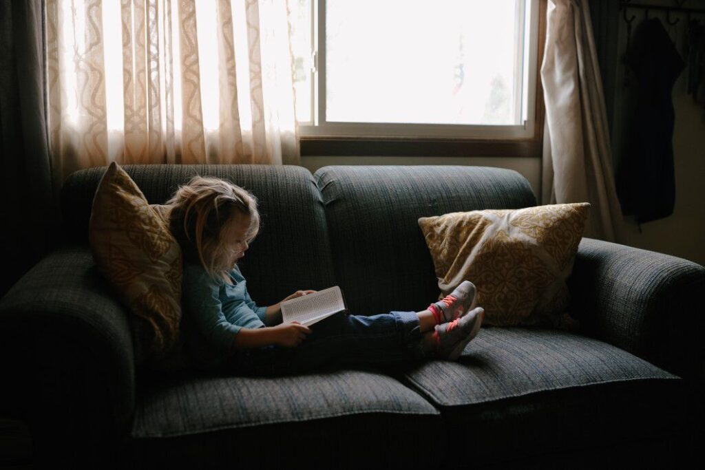 Menina lendo, sentada no sofá. Imagem ilustrativa texto dicas para leitura em família.