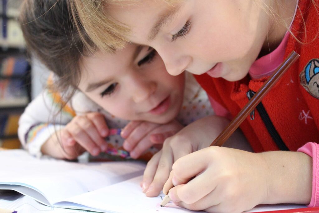 Meninas escrevendo juntas. Imagem ilustrativa texto ler em casa e na escola.